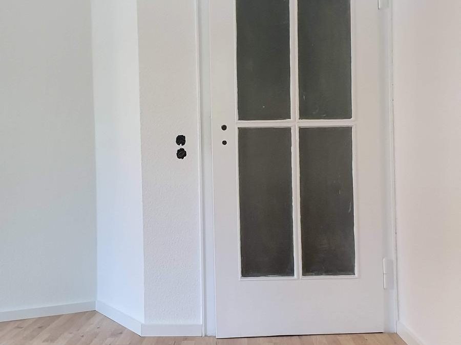 Renovierter Innenraum mit hellen Wänden, weißer Tür und Boden in Holzoptik.